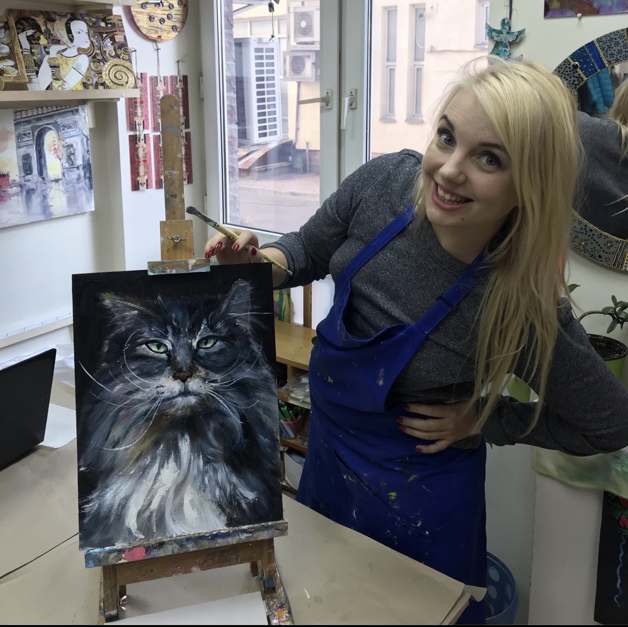 Marina Stognieva beside the completed Cat Herman painting, still wearing her working apron